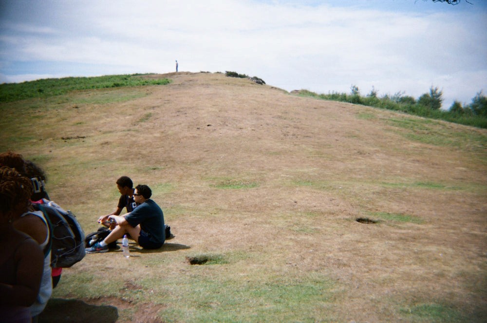 A group of women and non-binary people walk away from the camera up a trail in the countryside