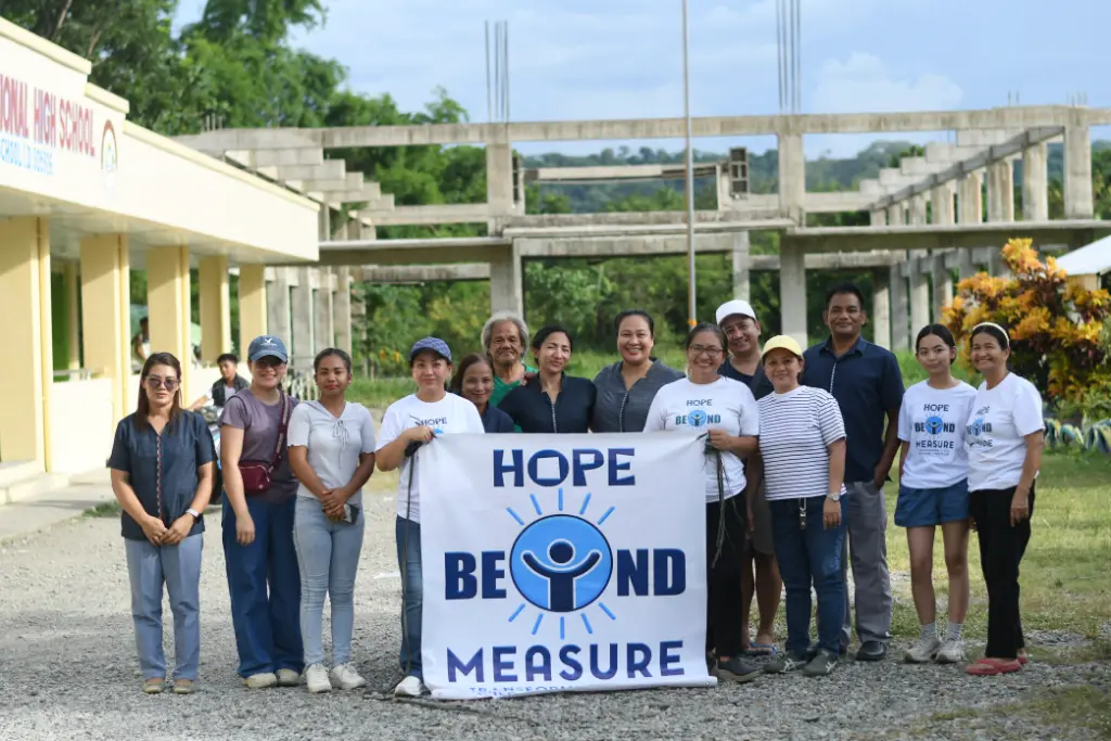 Volunteers and teachers holding the Hope Beyond Measure banner outside a school
