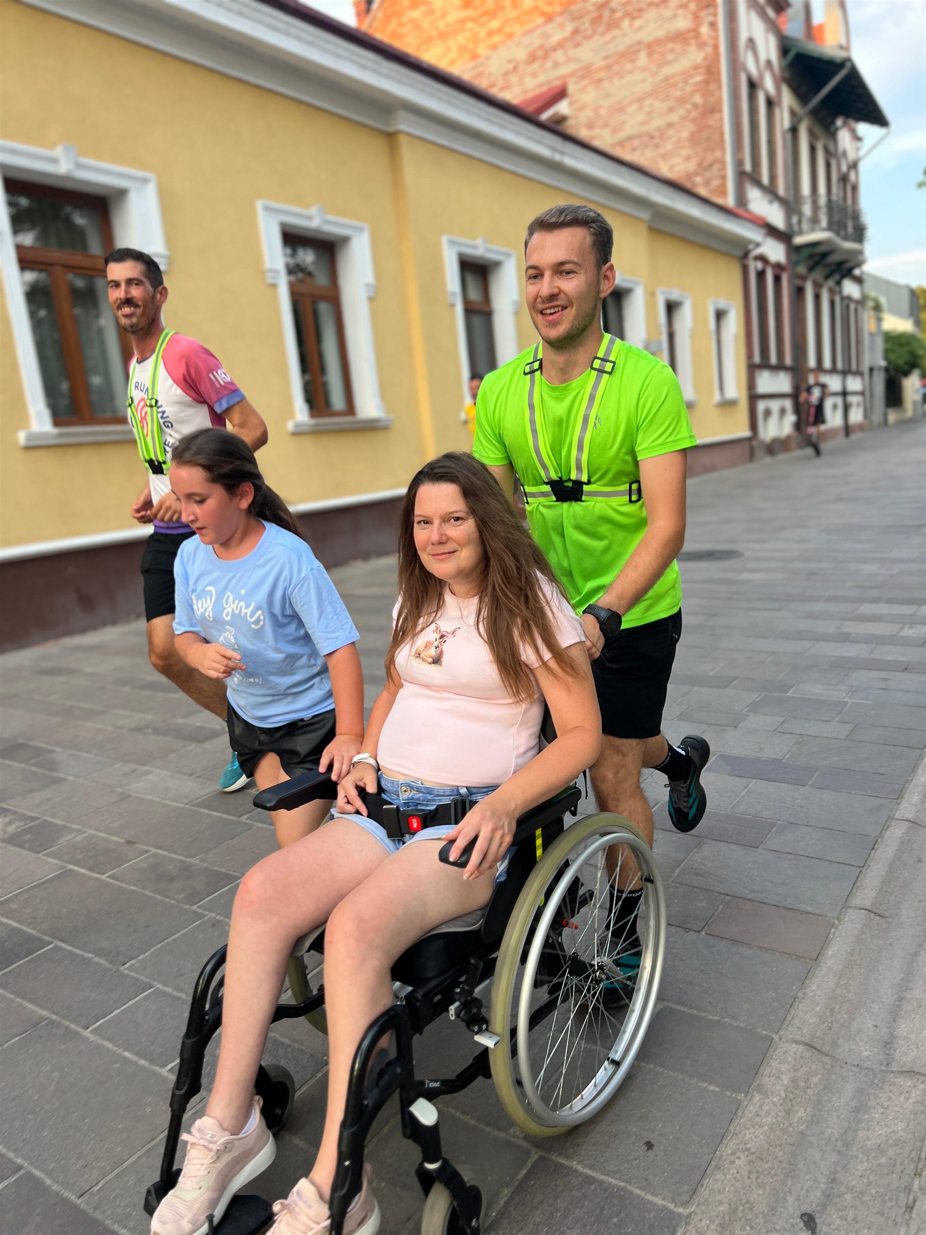 Tânără în scaun rulant participă la alergarea incluzivă, însoțită de alergători pe o stradă din Oradea.