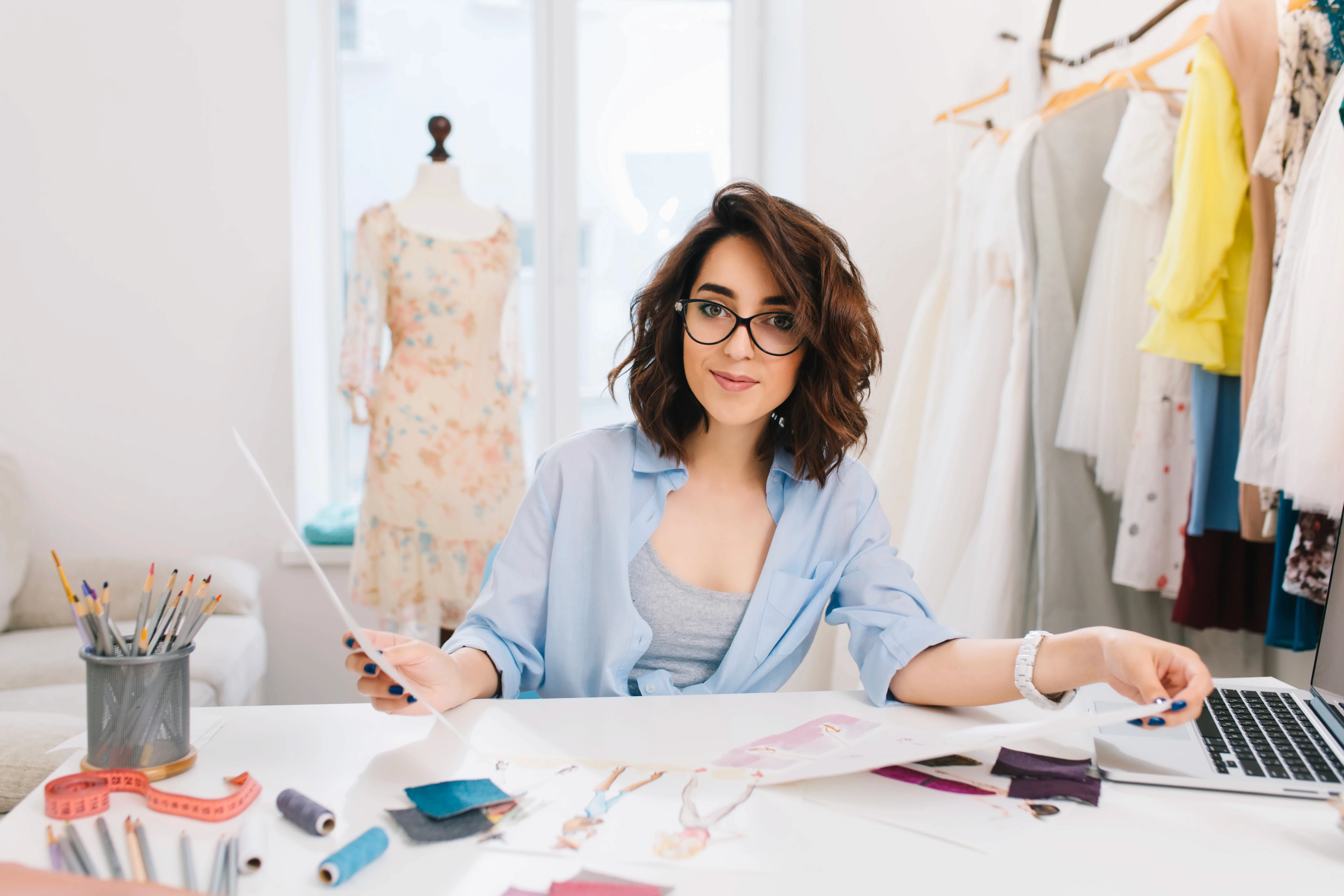 brunette-girl-is-sitting-table-workshop-she-holds-sketches-both-hands-looking-friendly-camera