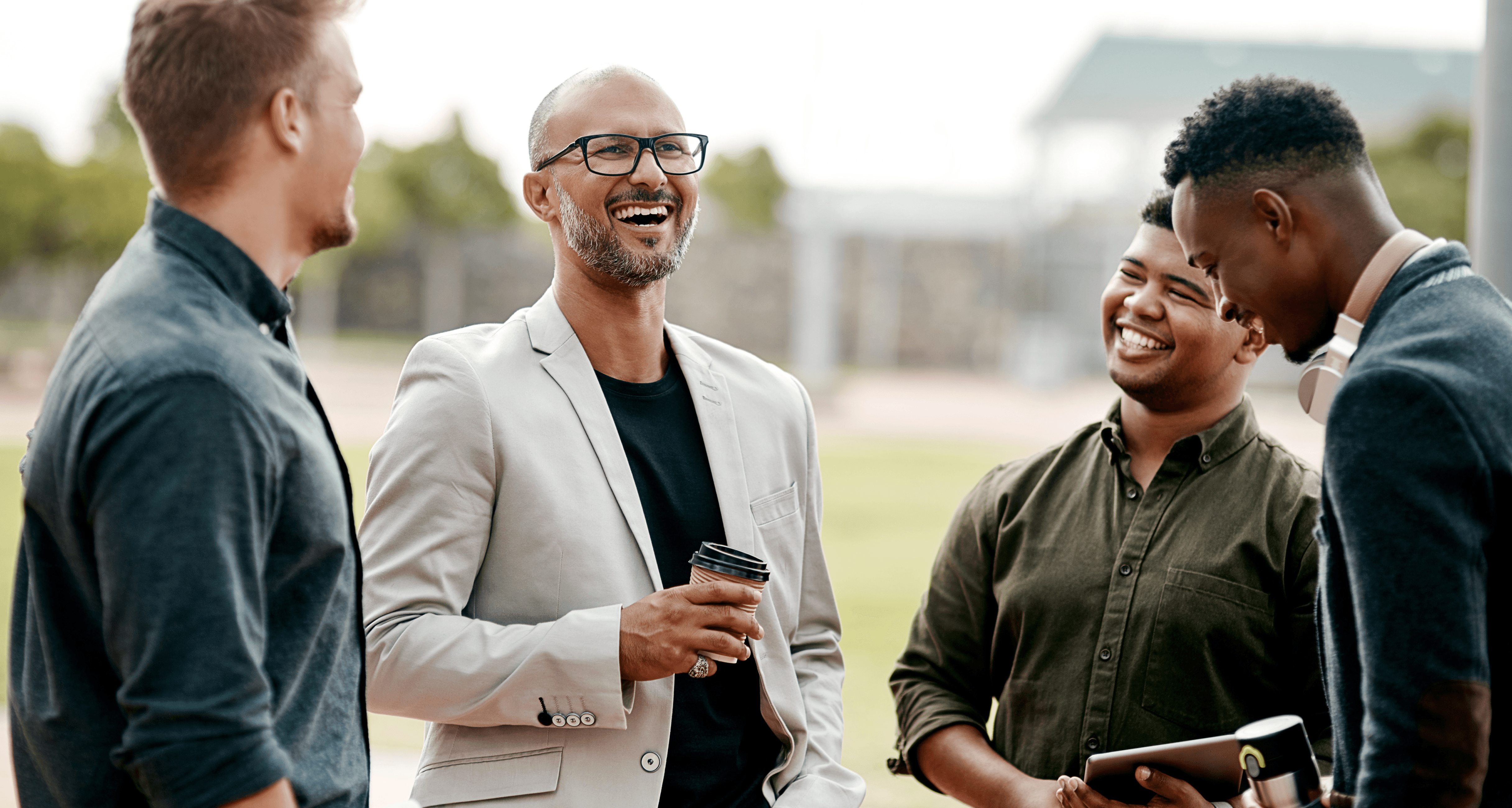 A group of diverse male colleagues laughing and talking during a coffee break outdoors.