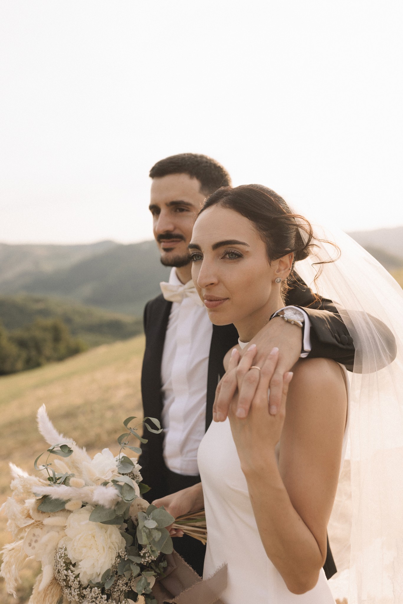 Sposi al Parco di Montebello in Toscana, lei in abito bianco e velo, lui in giacca scura, bouquet bianco in mano