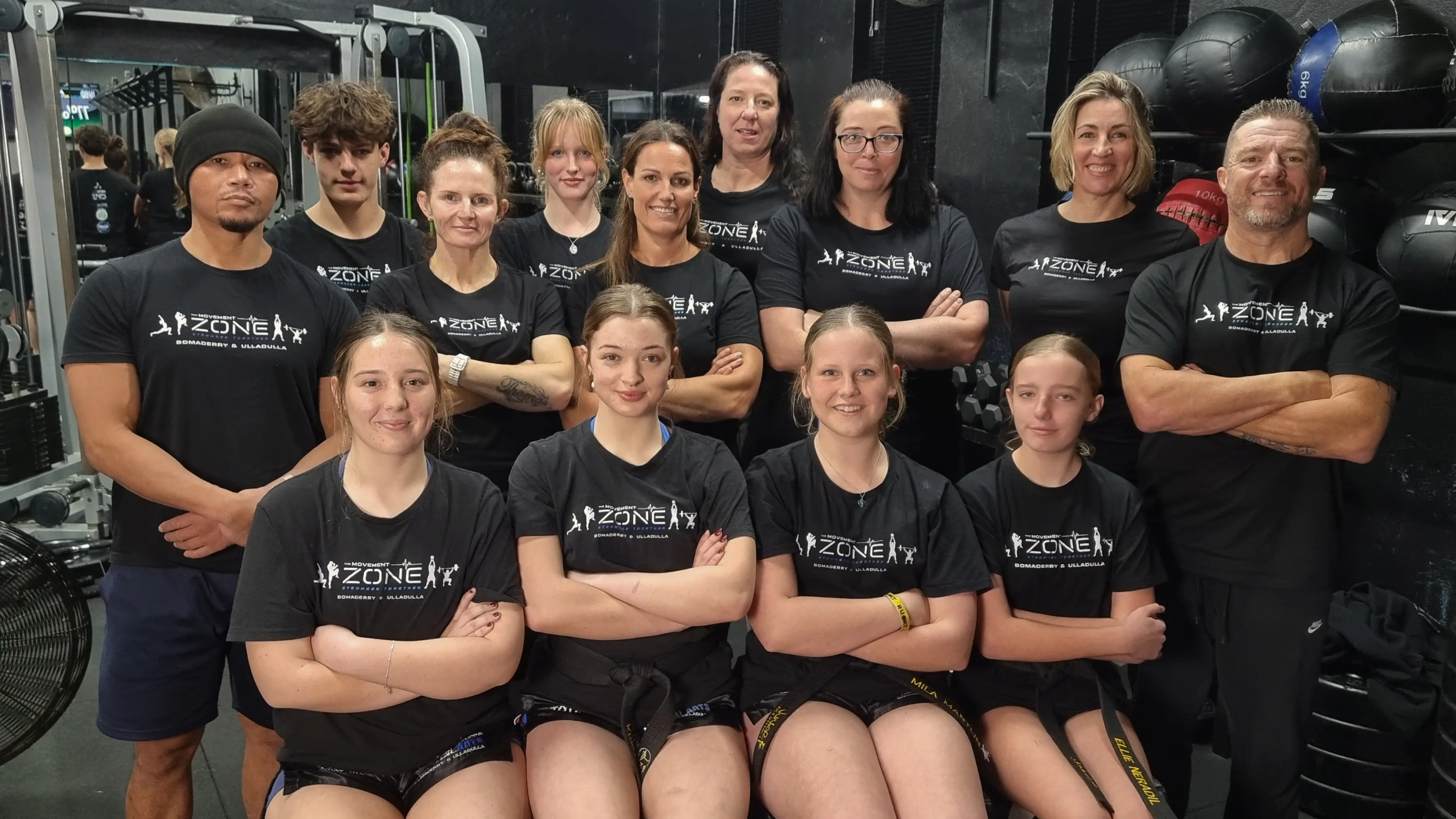 The Movement Zone coaching team smiling in front of gym wall, wearing branded shirts.