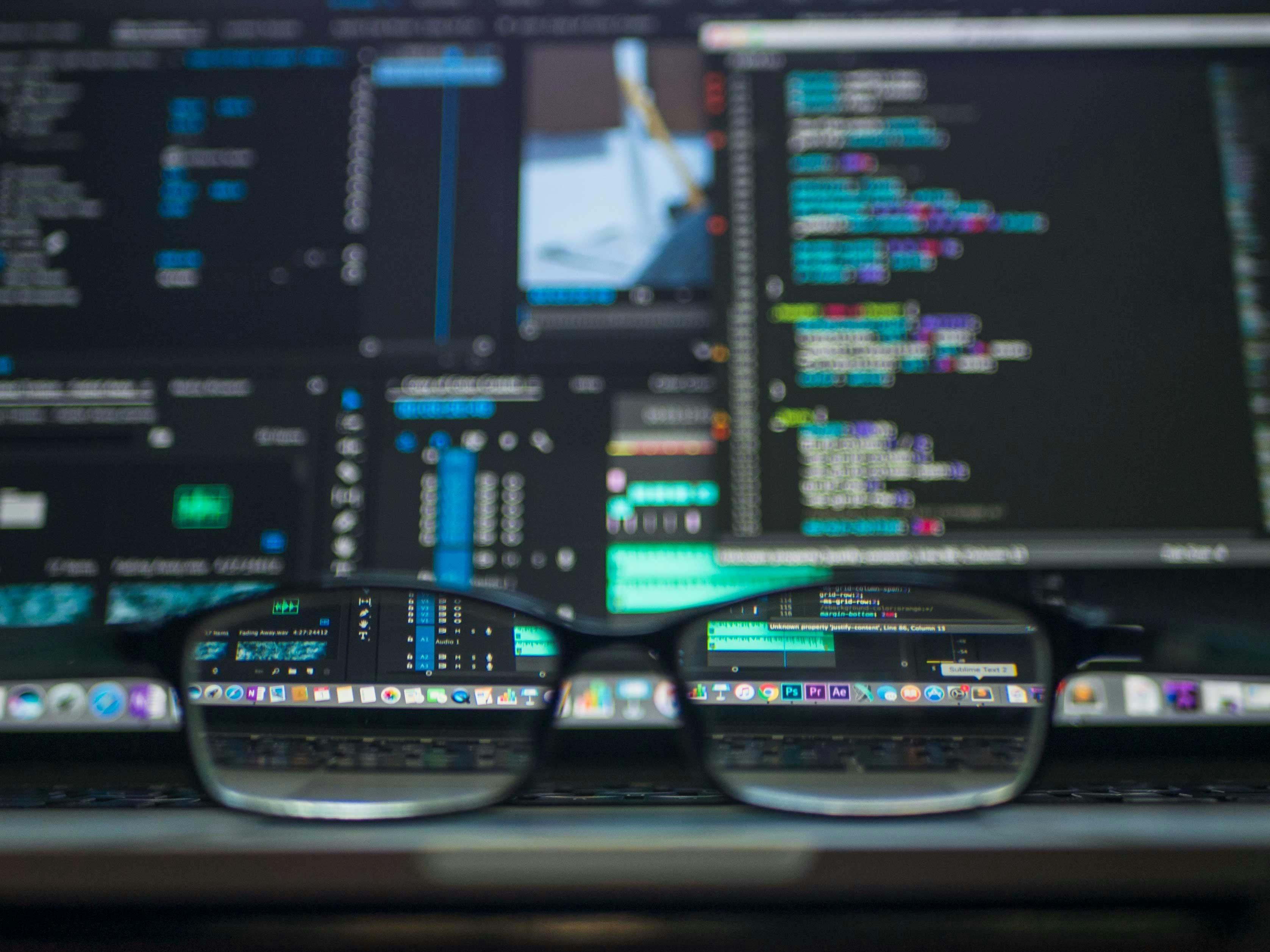 Blurred image of a computer screen with coding on and glasses that focusses the image through the lenses 