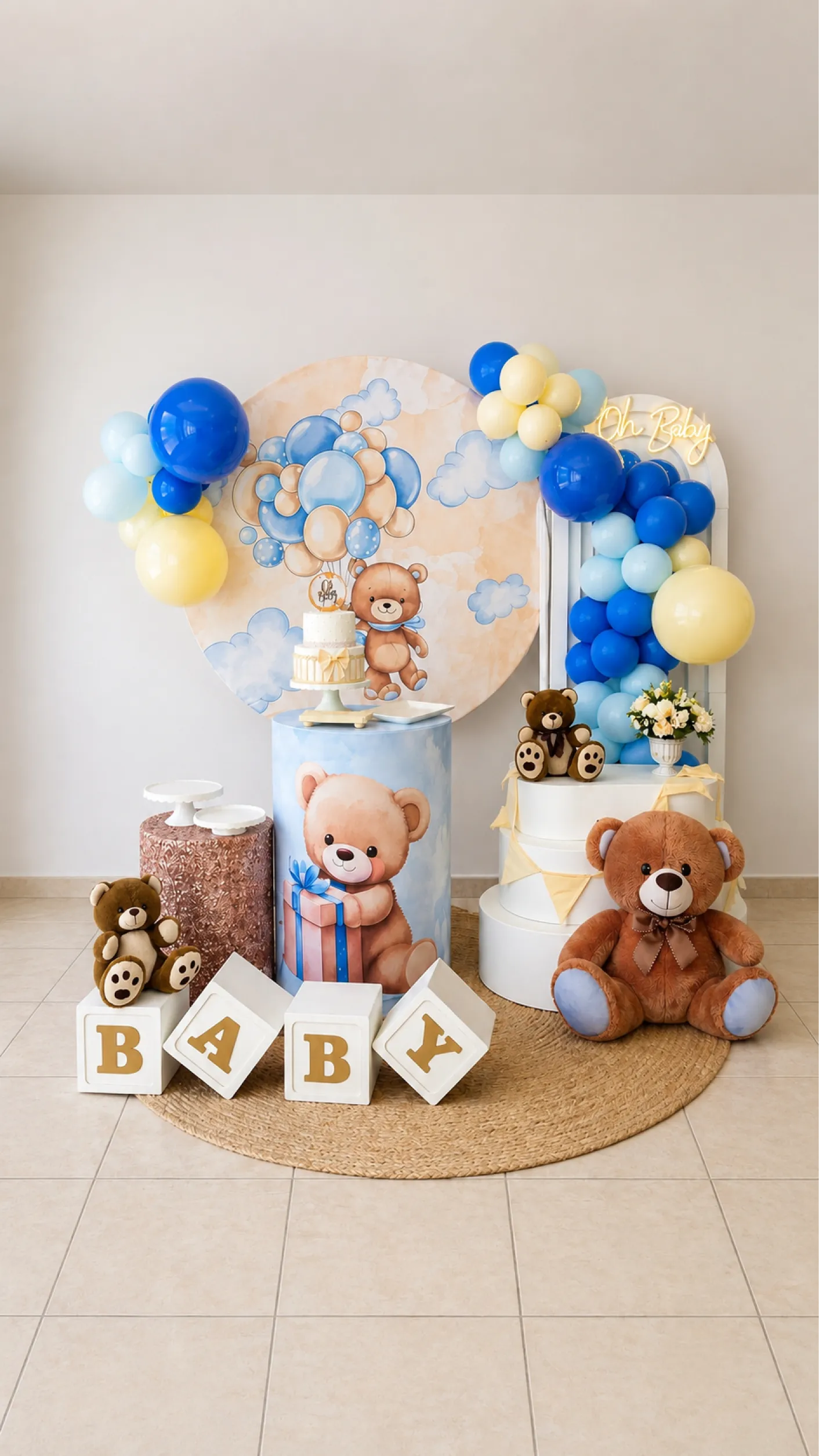 Decoração de chá de bebê com tema urso e nuvens, balões azuis e amarelos, painéis ilustrados, pelúcias e cubos com a palavra baby.