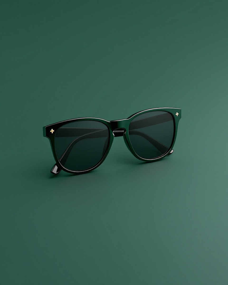 Sleek black sunglasses with dark lenses and gold accents positioned on a green surface. A stylish, modern vibe against a minimalist background.