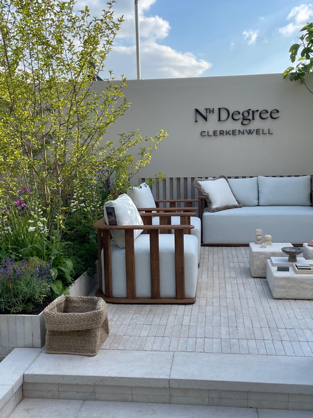 A cozy outdoor seating area with a sofa, cushions, and greenery against a light wall and blue sky.
