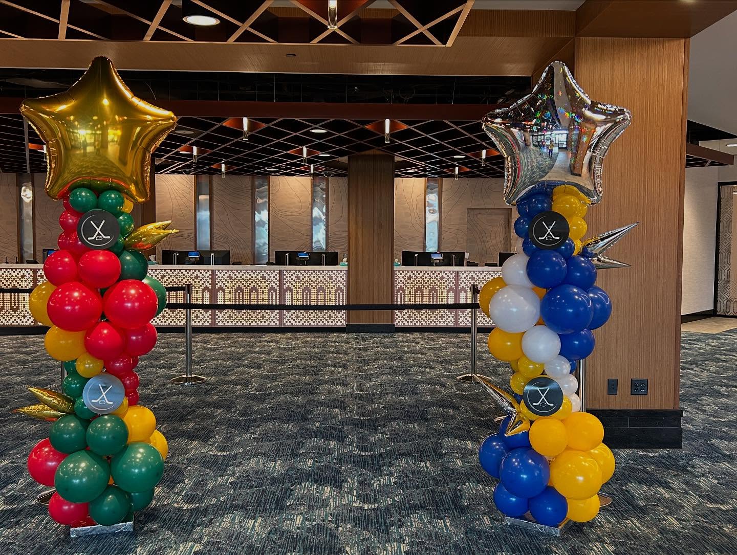 Red and blue balloon columns with yellow star toppers placed on either side of a stage or presentation area created by Be Bold Balloons