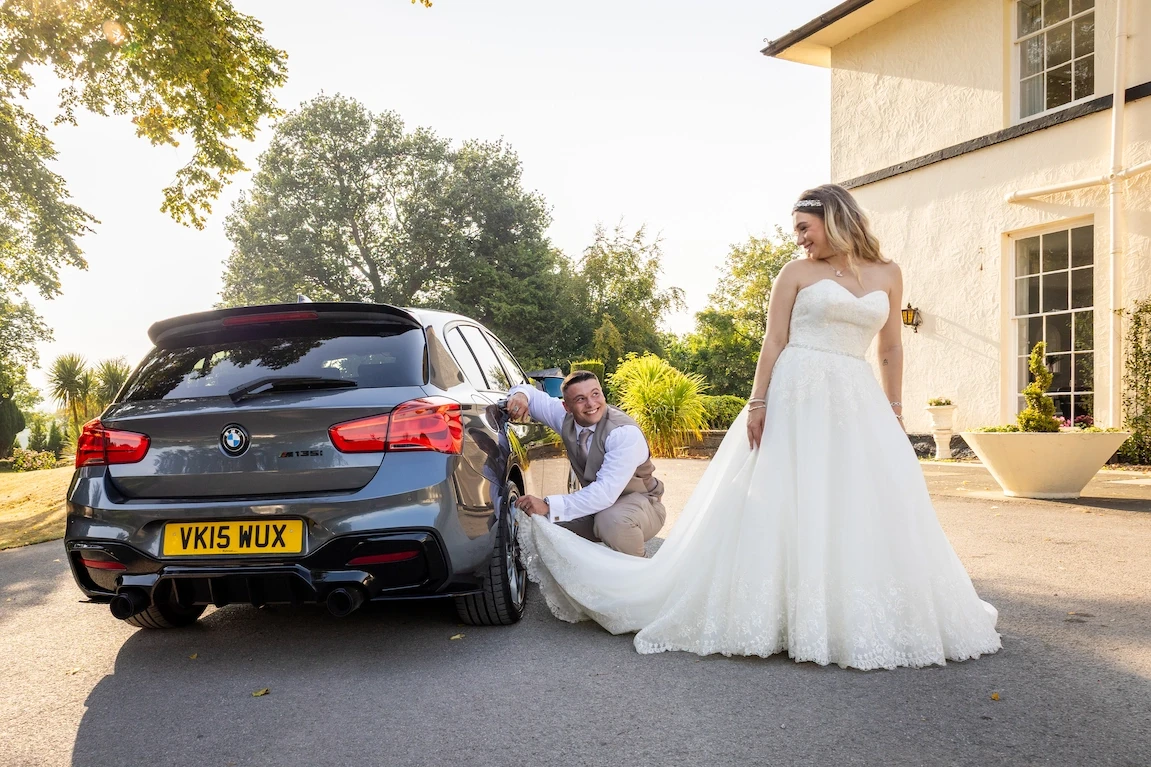 Lauren and Ethan laughing together beside their wedding car outside Highfield Hall
