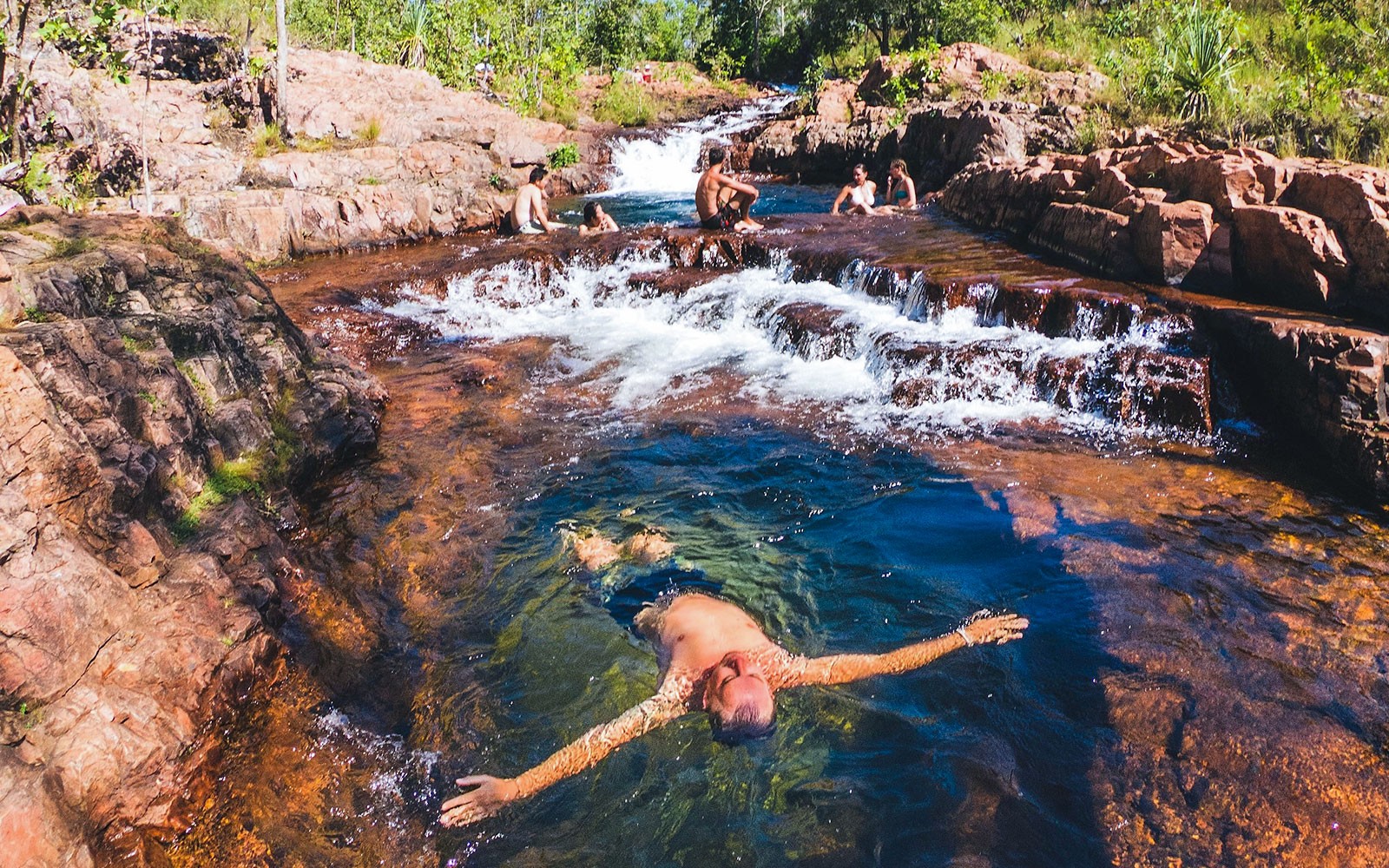 Visitors swimming in a natural pool at Litchfield National Park, surrounded by rocky terrain.