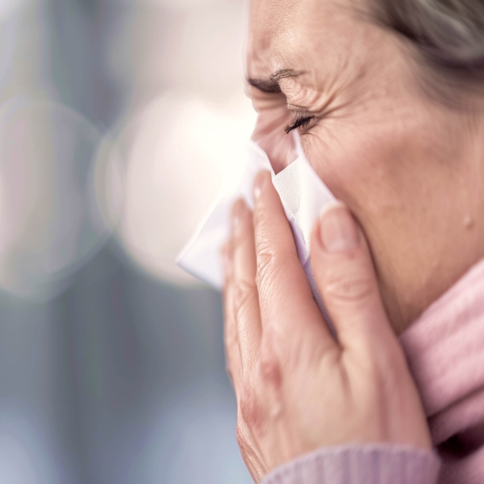 Gesichtsdetail einer Frau, die sich gerade die Nase putzt