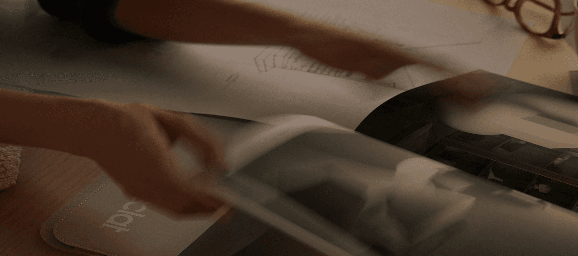 Blurred close-up of hands flipping through architectural plans and a photo book on a desk