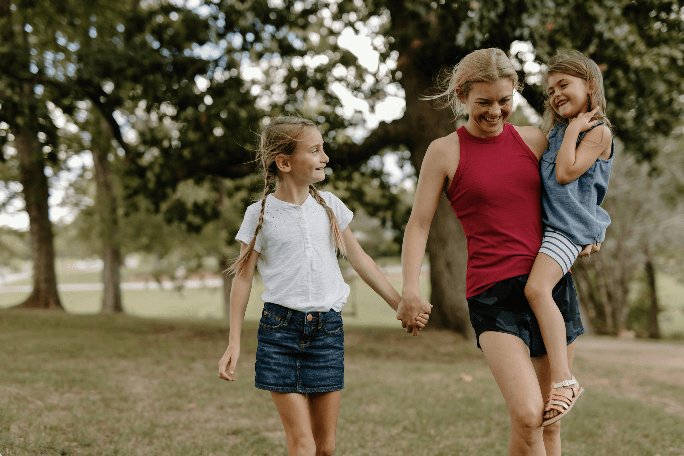 woman carrying young girl while older girl walks alongside them
