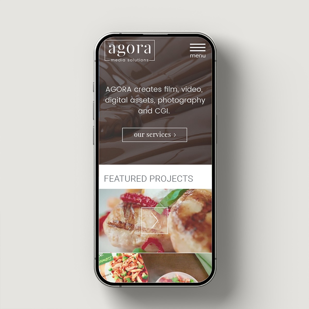 Mobile phone displaying Agora Media Solutions responsive website with chocolate background and featured projects preview.