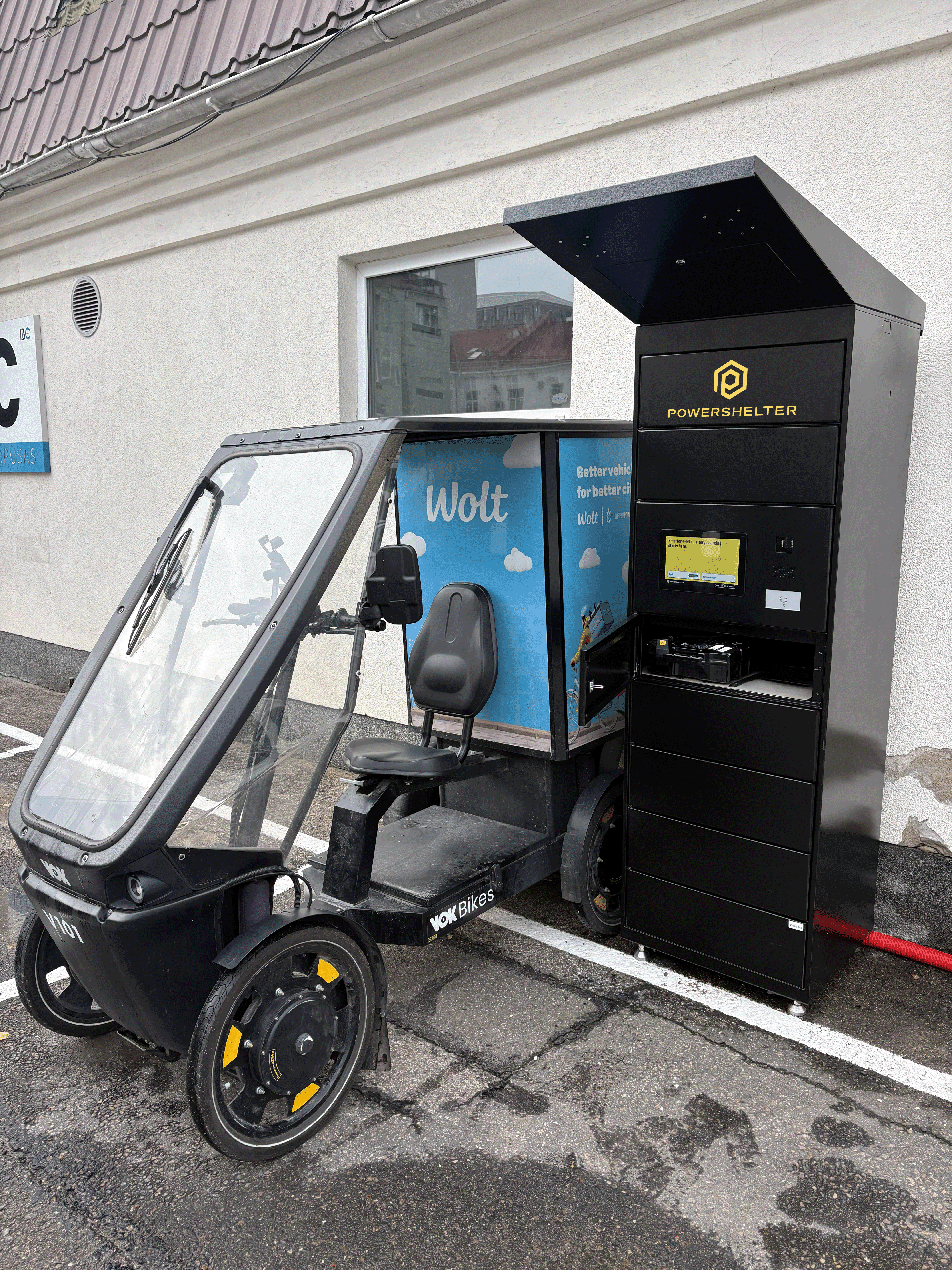 A person placing an e-bike battery into a charging locker, with charging cables connected and a digital display visible on the locker unit.