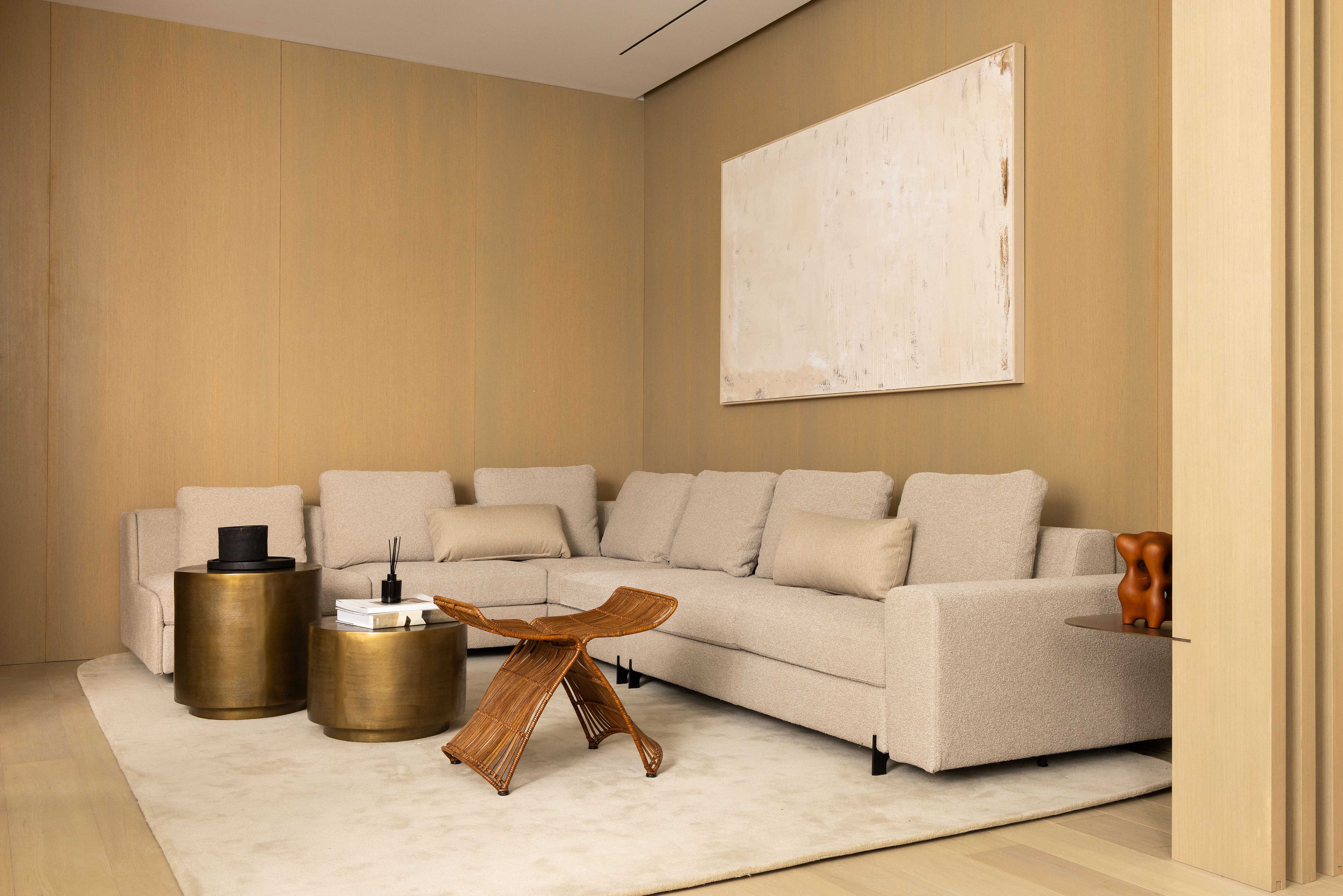 Salon vu de face avec canapé d'angle beige, tables basses en laiton et tableau blanc