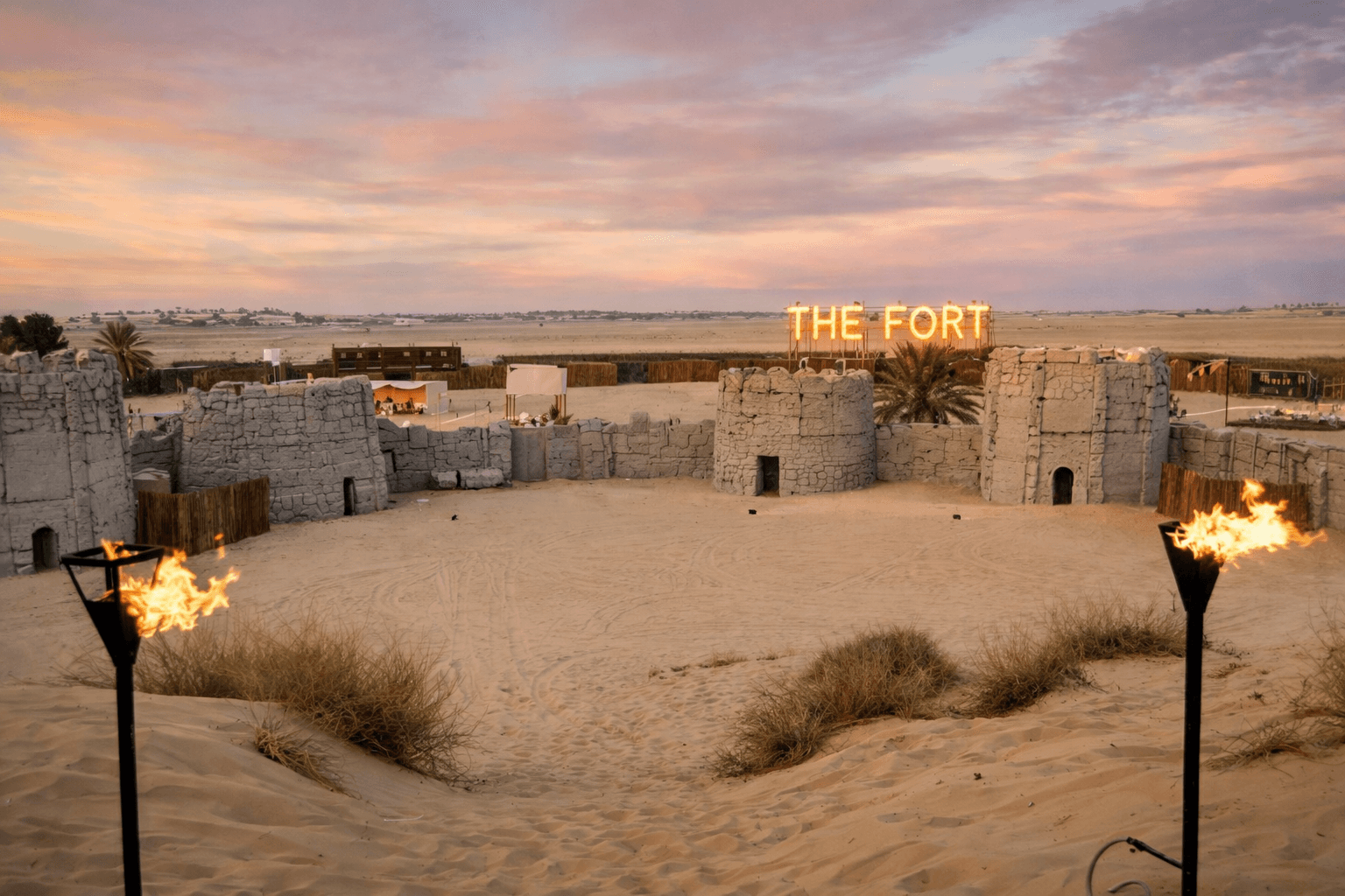 An aerial view of the stone-walled Fort Al Lisaili desert camp in Dubai, featuring a traditional Arabian arena under a sunset sky for Dune Quest Tours.