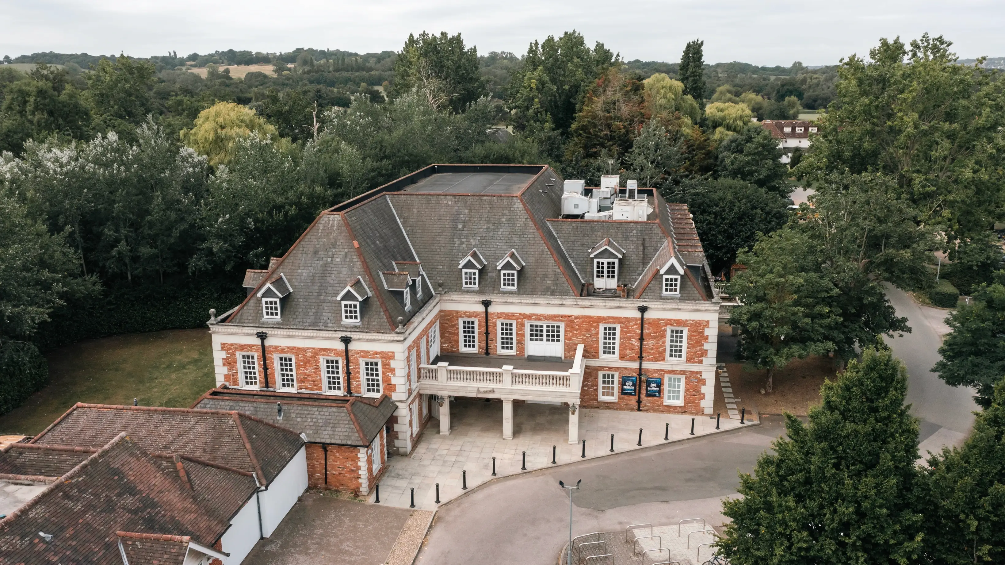 Brick building with dormer windows surrounded by trees.