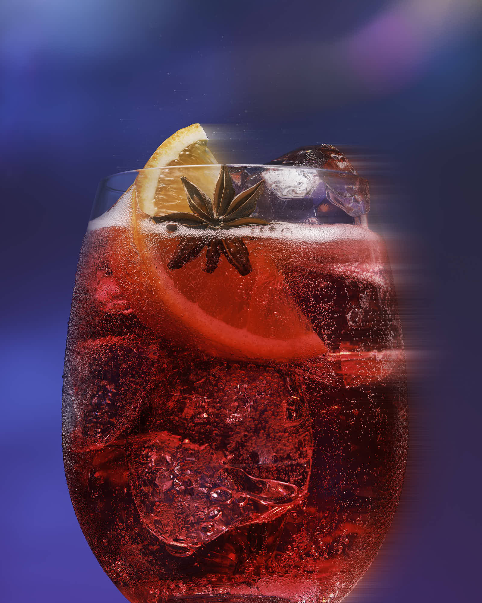 A close-up of a glass filled with dark red liquid, ice, and a slice of orange, set against a colorful background.