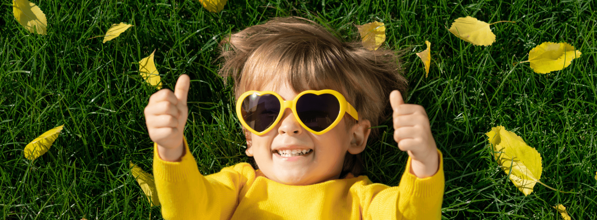 Enfant allongé dans l'herbe. Lunette en forme de coeur. Habillé tout en jaune