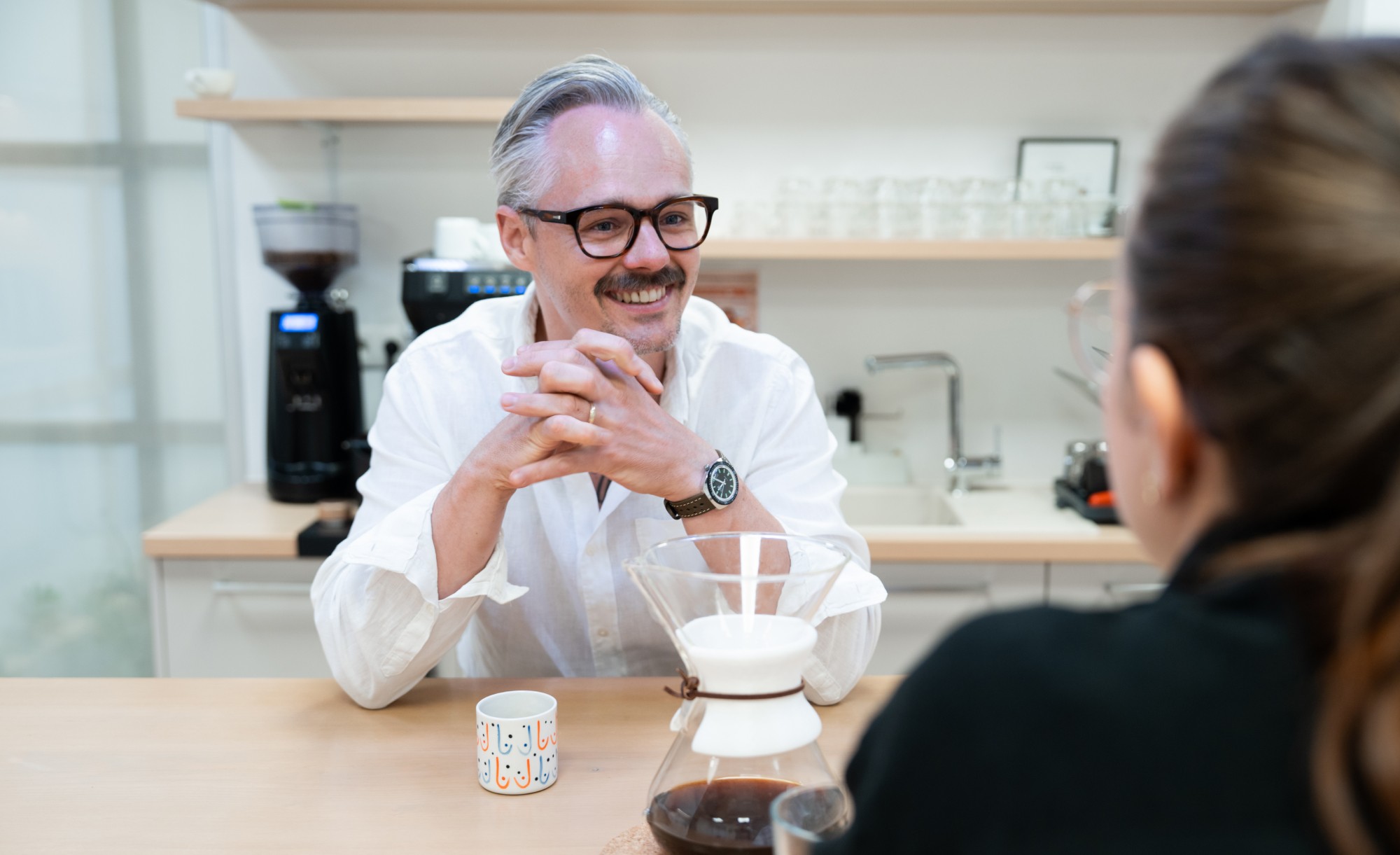 Lukáš Rychtecký sitting at a table, talking to a colleague over a cup of filtered coffee