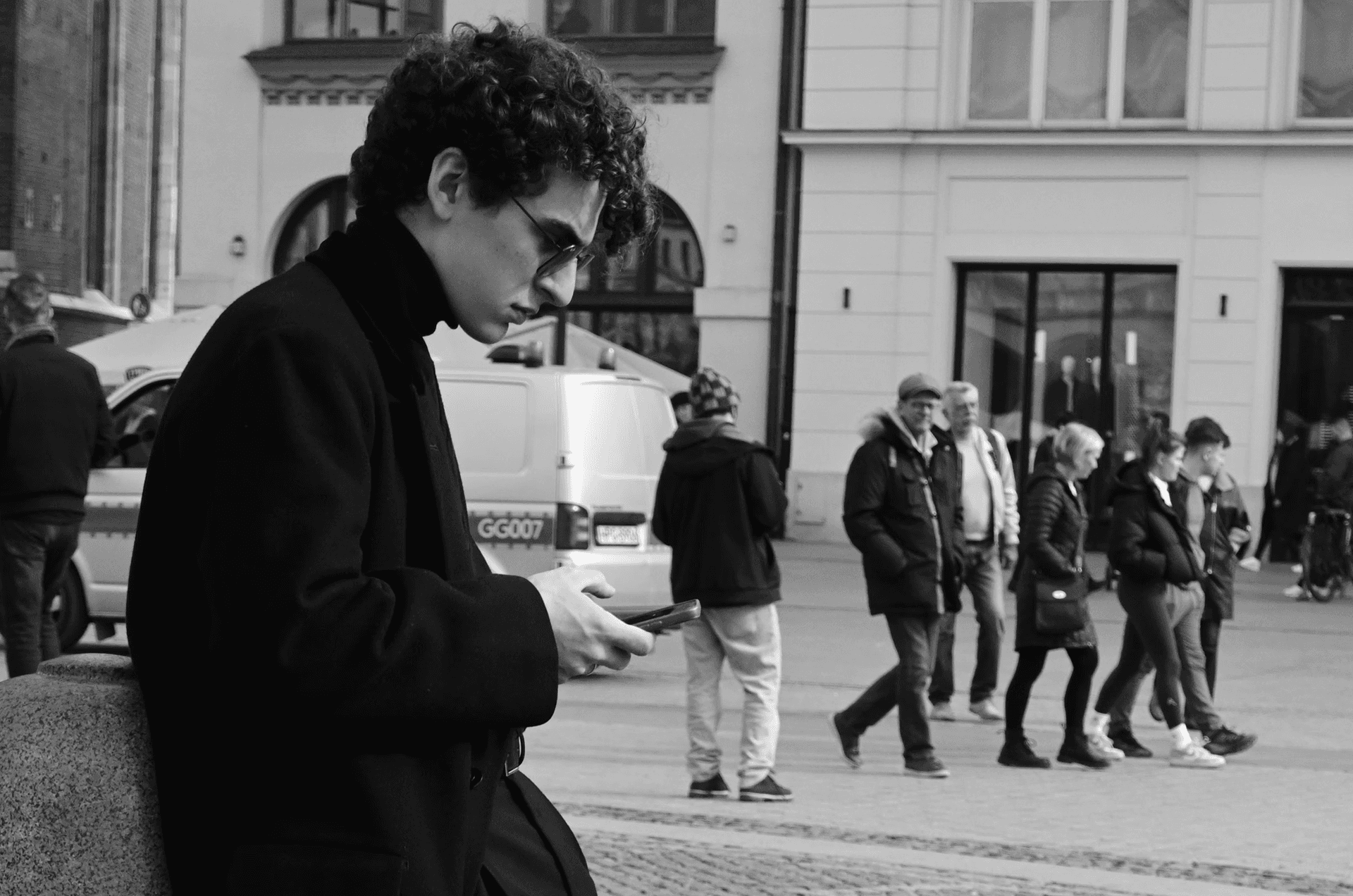 A monochrome street scene with one foreground figure holding a phone, symbolizing how B2B buying committees decide in 2026.