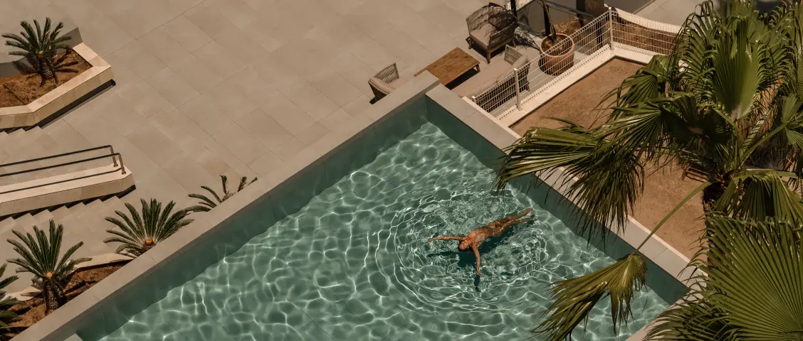 Frau schwimmt entspannt in einem modernen Pool mit Palmen