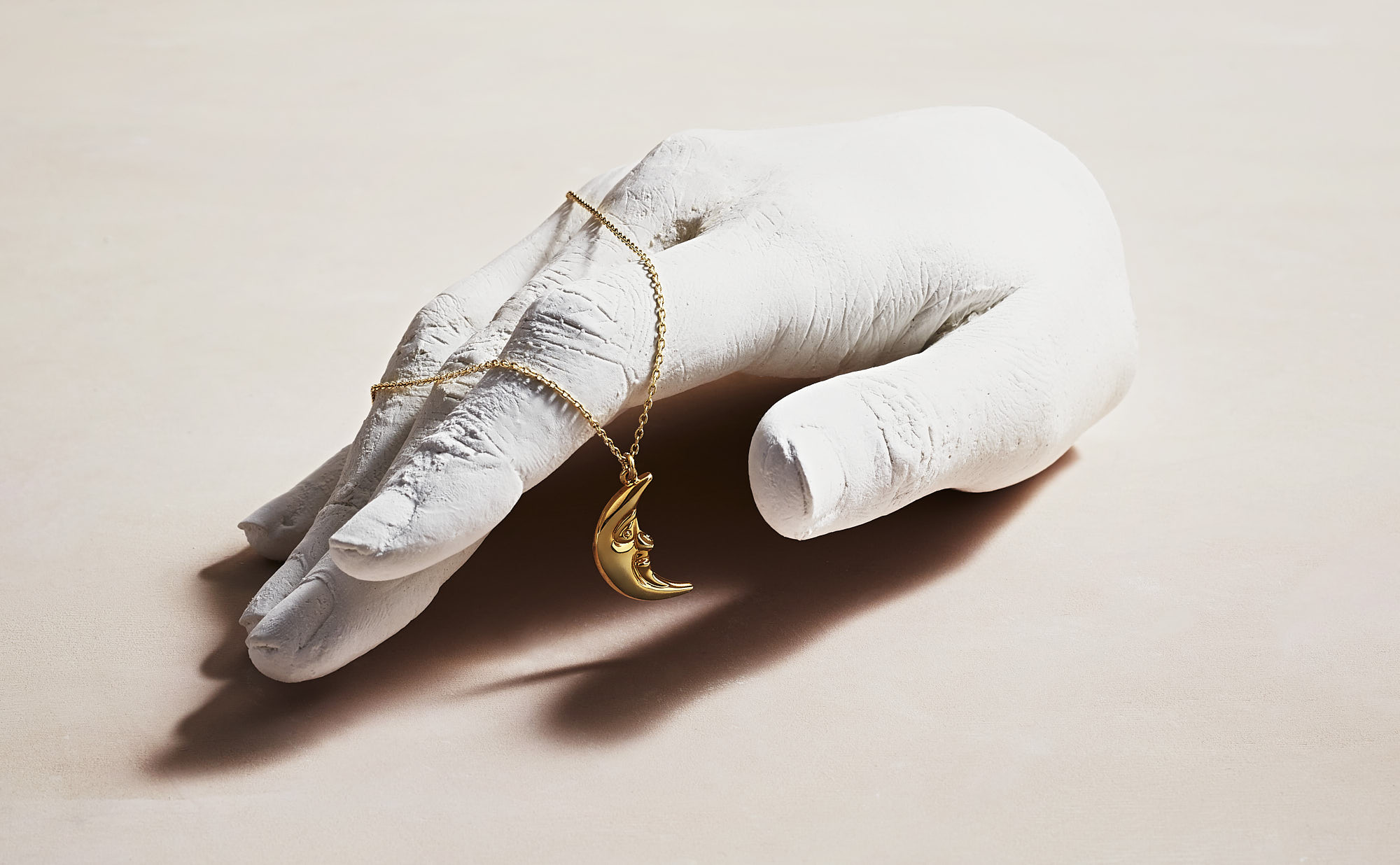 Gold moon necklace on a white plaster hand sculpture, elegant jewelry display.