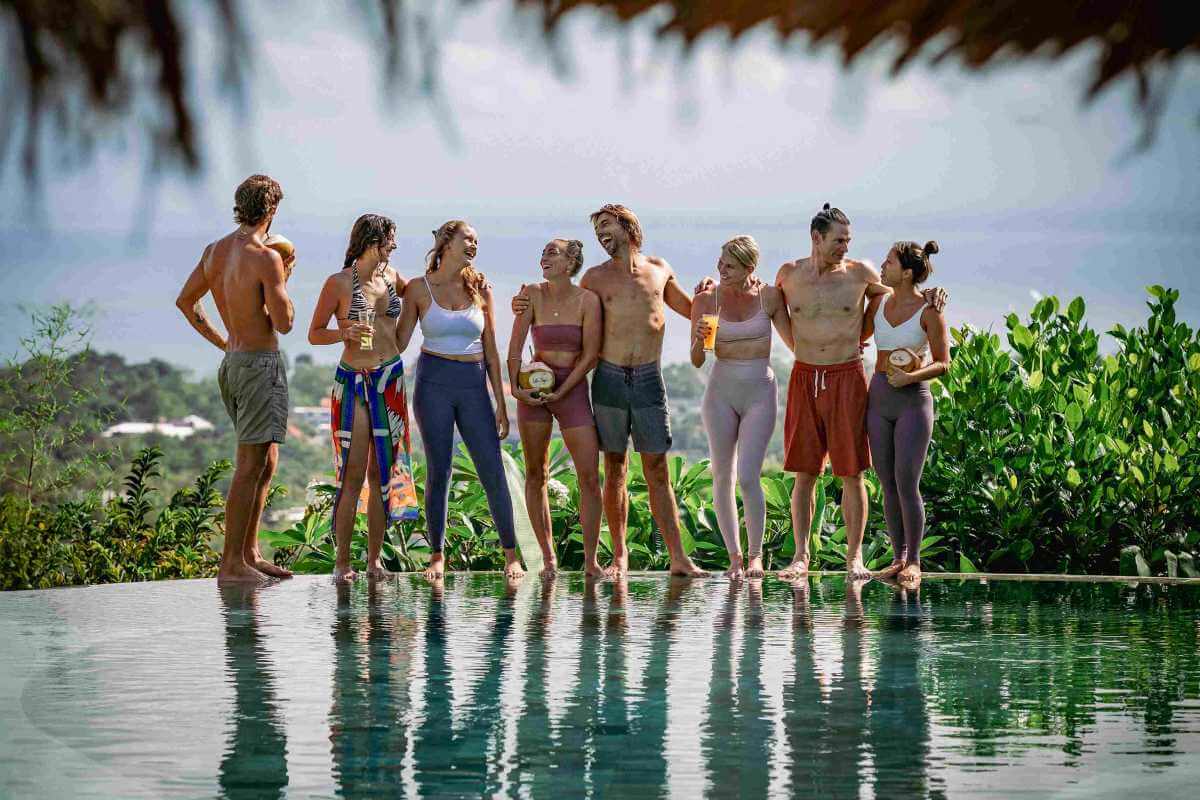 Happy yoga teacher training group socializing by the infinity pool overlooking the ocean in Bali.