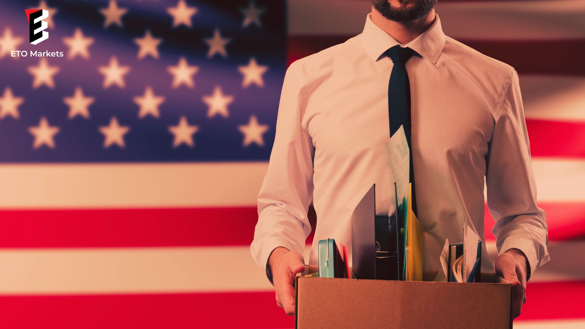 A man holding a work kit stands in front of a US flag, symbolizing job opportunities in the USA.