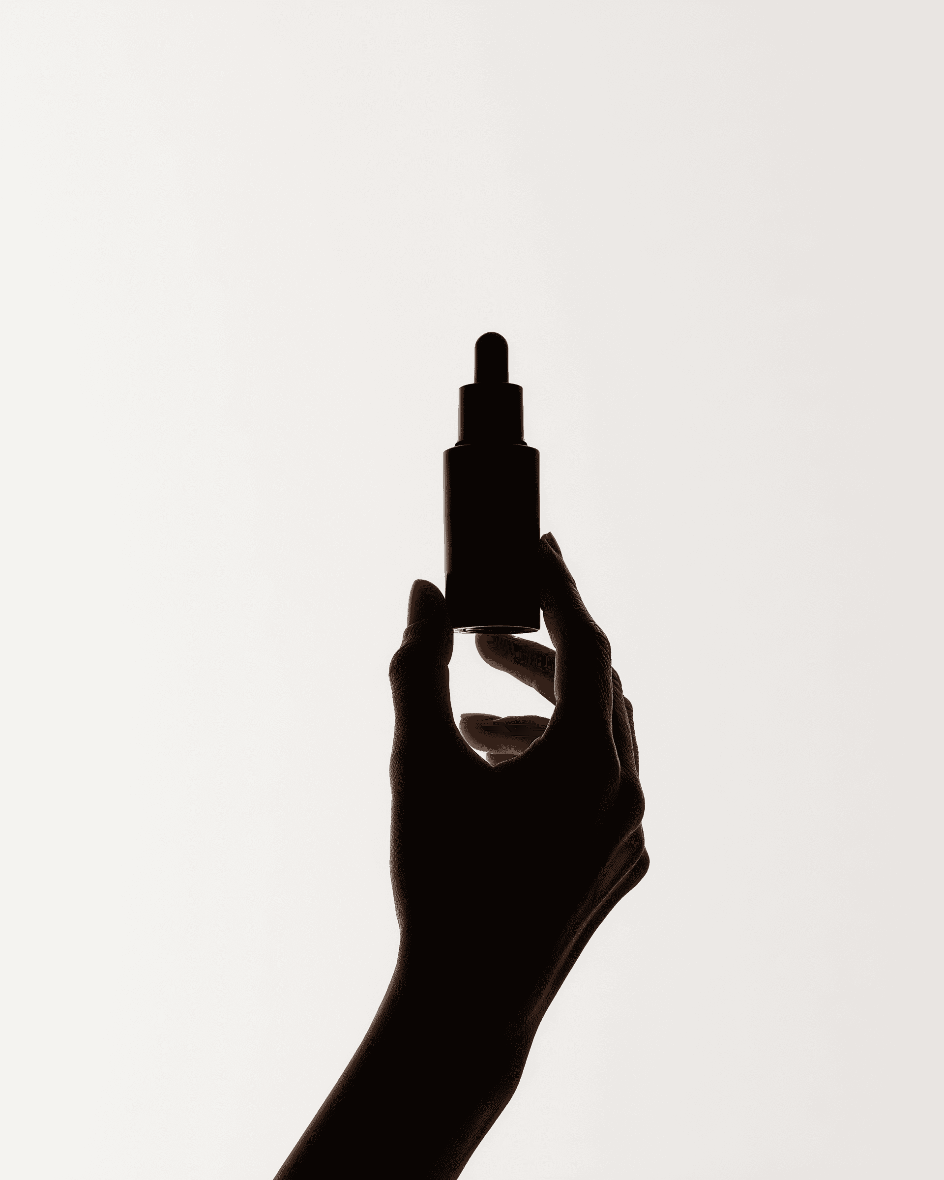 Hand holding black dropper bottle in silhouette