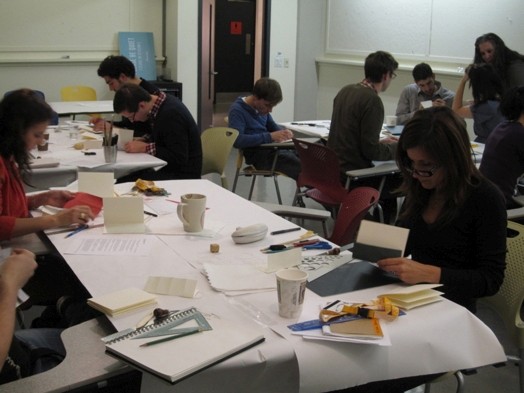 A photo of a group of students learning how to fold paper using different office items.