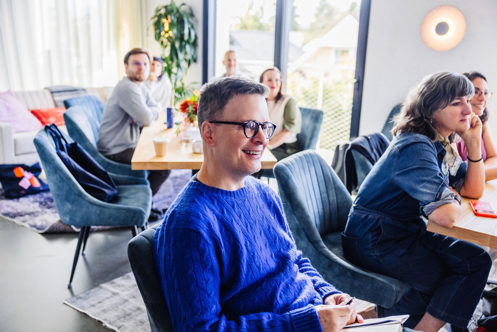 People seated and smiling while listening during a group meeting in a bright, modern room.