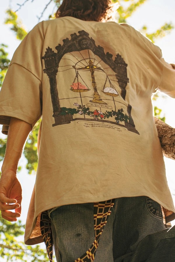 Parkour athlete wearing a beige t-shirt with a graphic design on the back, standing outdoors with trees in the background.