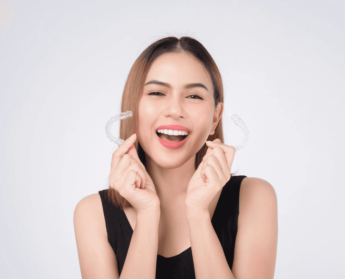Invisalign in Dubai with a woman smiling confidently, holding her clear aligners, highlighting discreet and effective treatment.