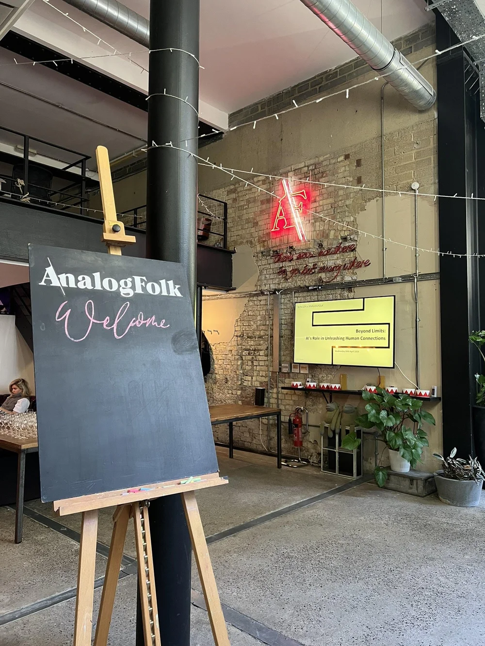 A wooden signboard outside a building, with text, and colorful decorations inside visible through the entrance.