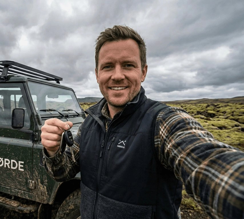 Smiling man holding a car key in a green, natural setting.