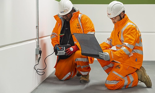 Modern glass building with illuminated facade and trees at sunset