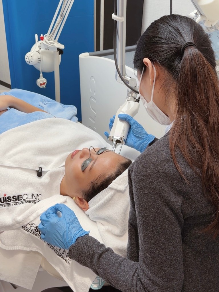 A female patient receiving a Pico Laser facial treatment at Suisse Clinic, with a medical professional using a handheld laser device on her forehead.
