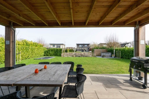 Het uitzicht vanaf de houten veranda over de eettafel naar de tuin.