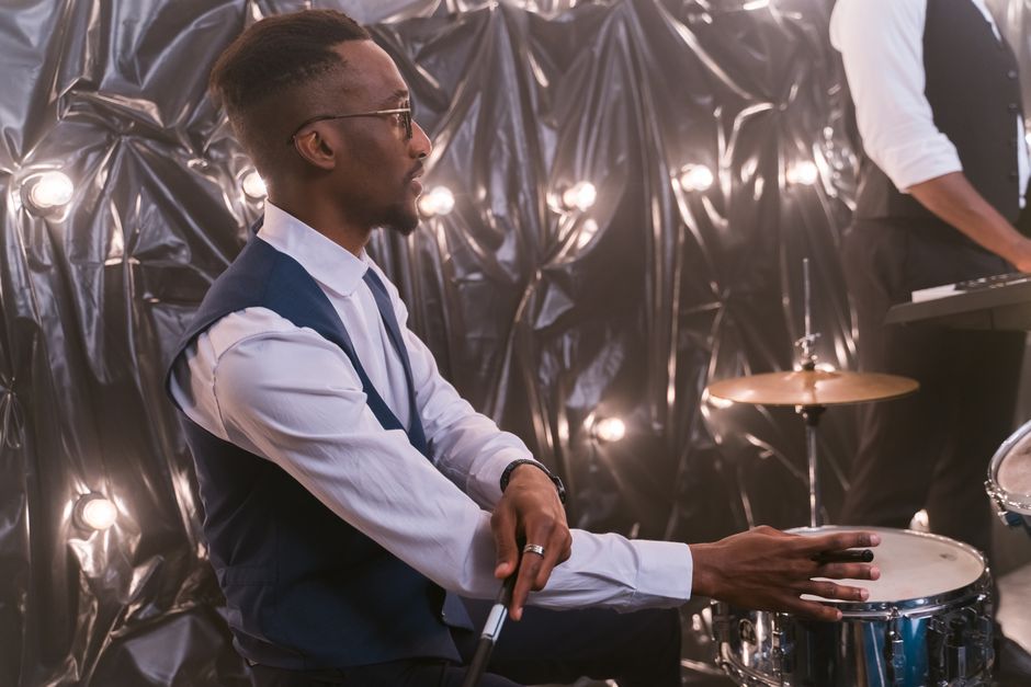 Side view of a skilled drummer performing live under stage lights, adding rhythm to the music.