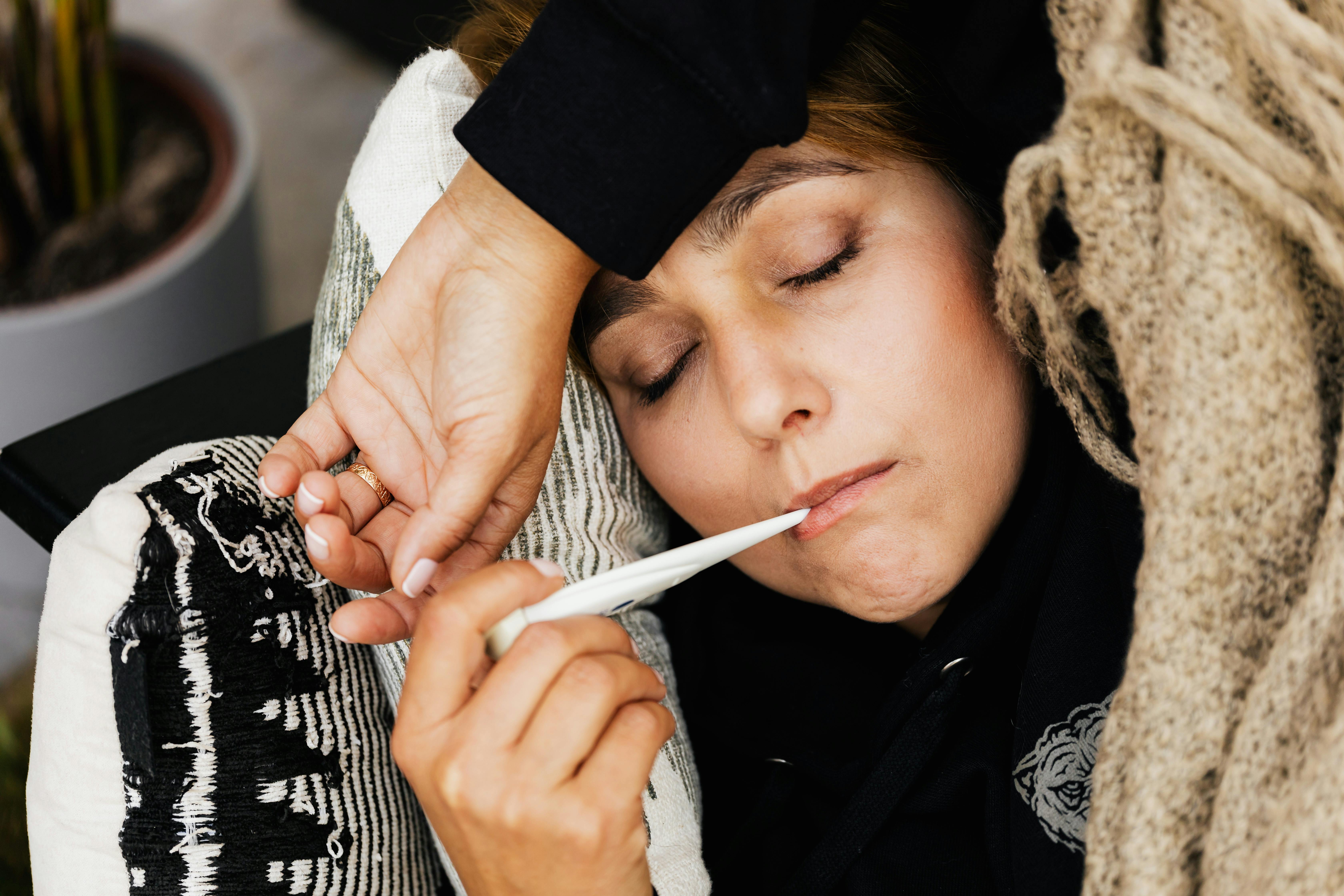 A Woman Taking Her Temperature with a Thermometer because she has a fever