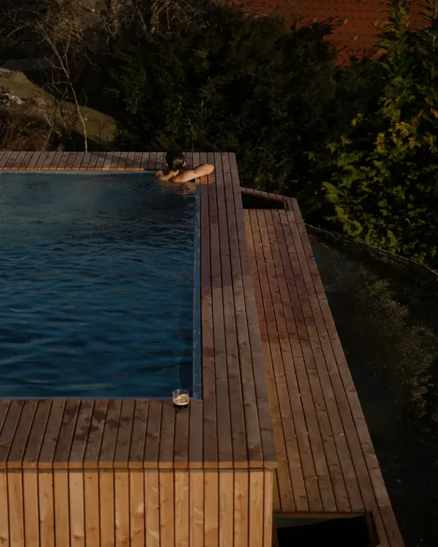 Person schwimmt am Rand des Pools, umgeben von Holzdeck und Bäumen