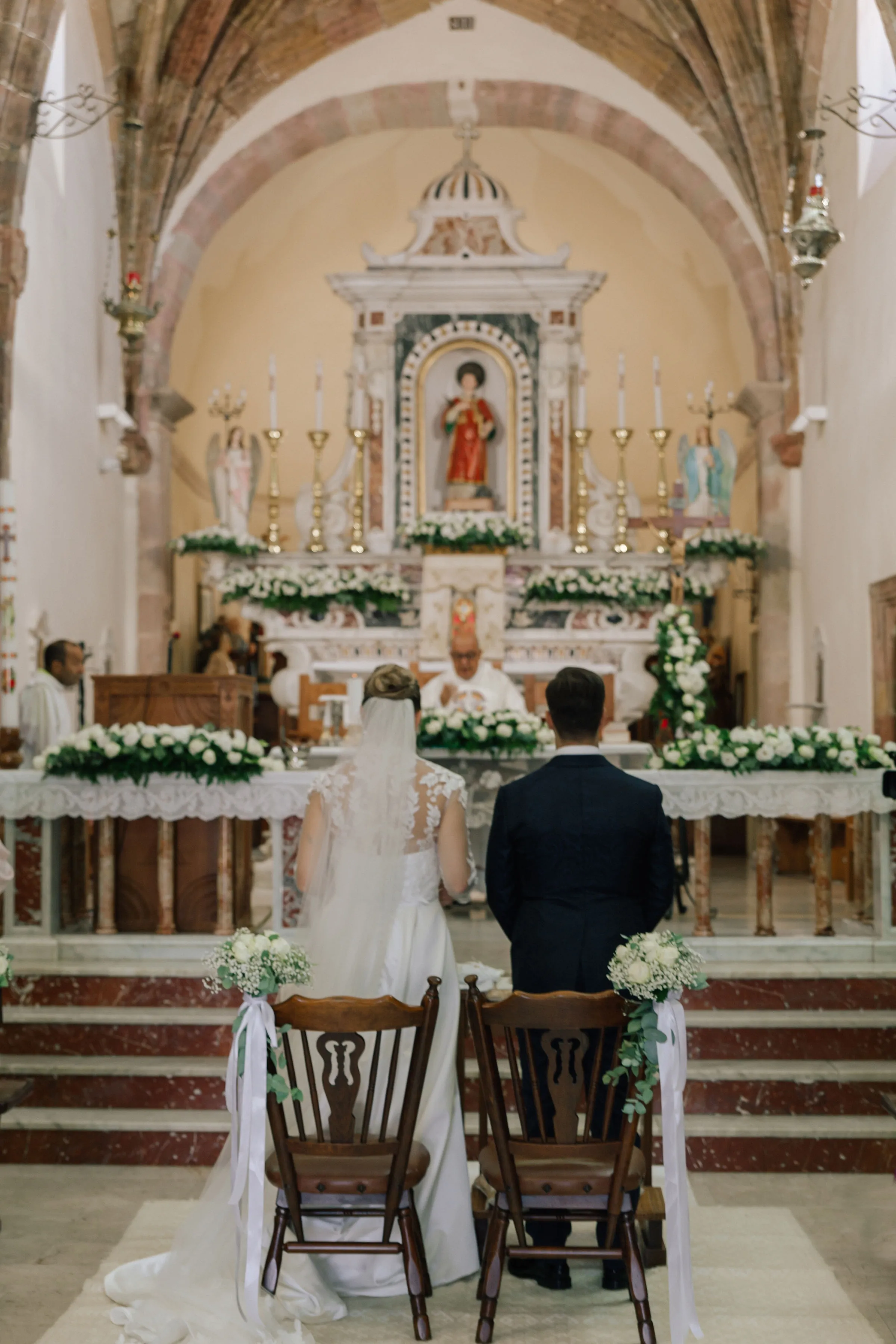 A couple in wedding attire walks hand in hand across a sunlit field.