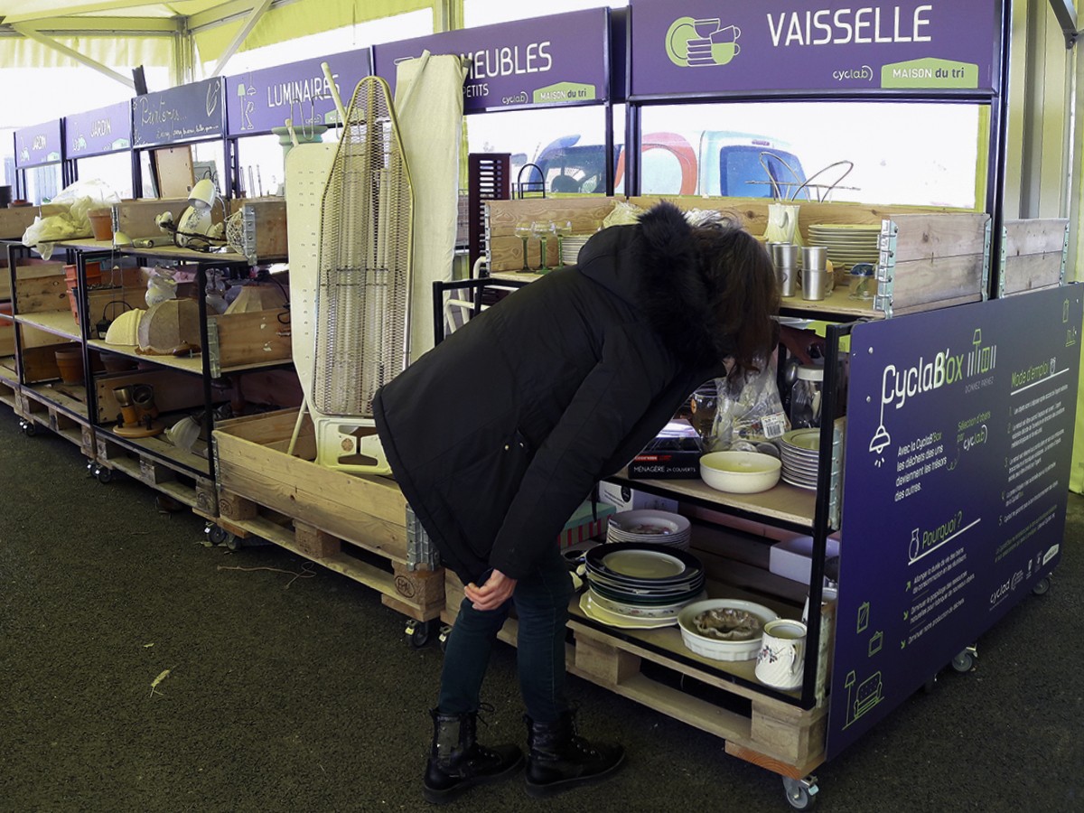 Stand de collecte de vaisselle CyclaBox dans un espace de tri, avec une personne inspectant des assiettes en céramique