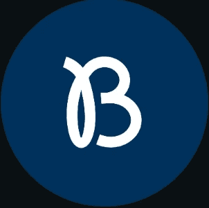 A young man with light brown hair is wearing a black suit jacket and white shirt, standing in a softly lit office setting, conveying professionalism.