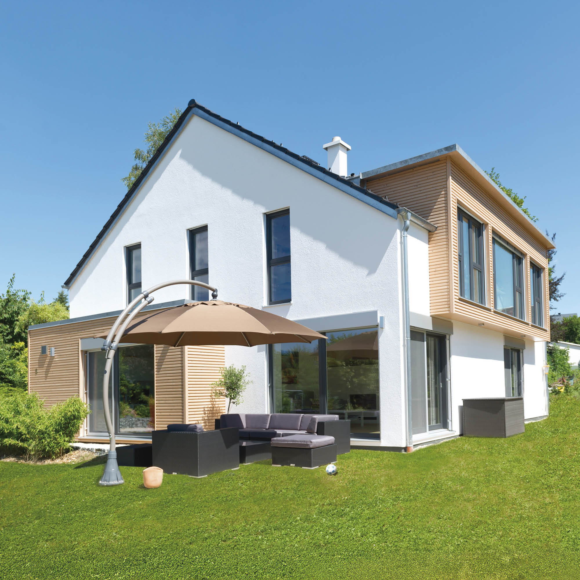 Modernes weißes Haus mit Holzapplikationen, große Fensterfronten und eine Terrasse mit Lounge-Möbeln und Sonnenschirm.