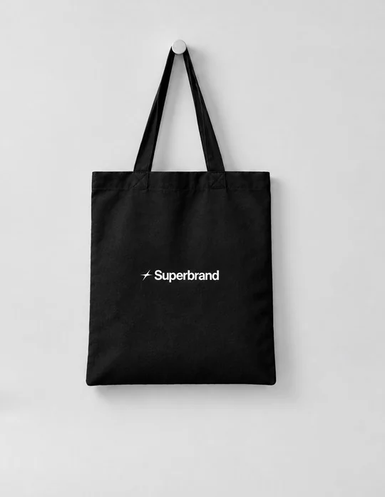 A black Superbrand tote bag hanging on a wall.