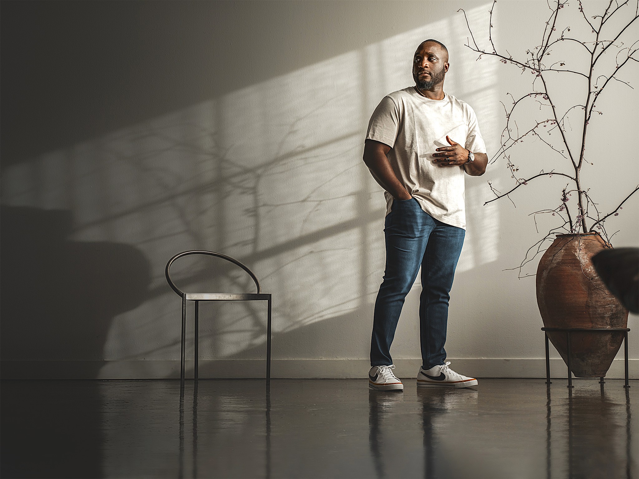 Tade Bolarin, executive and life coach for ambitious professionals, standing in a Japandi minimalist loft, wearing casual beige t-shirt, blue jeans, and Nike shoes.