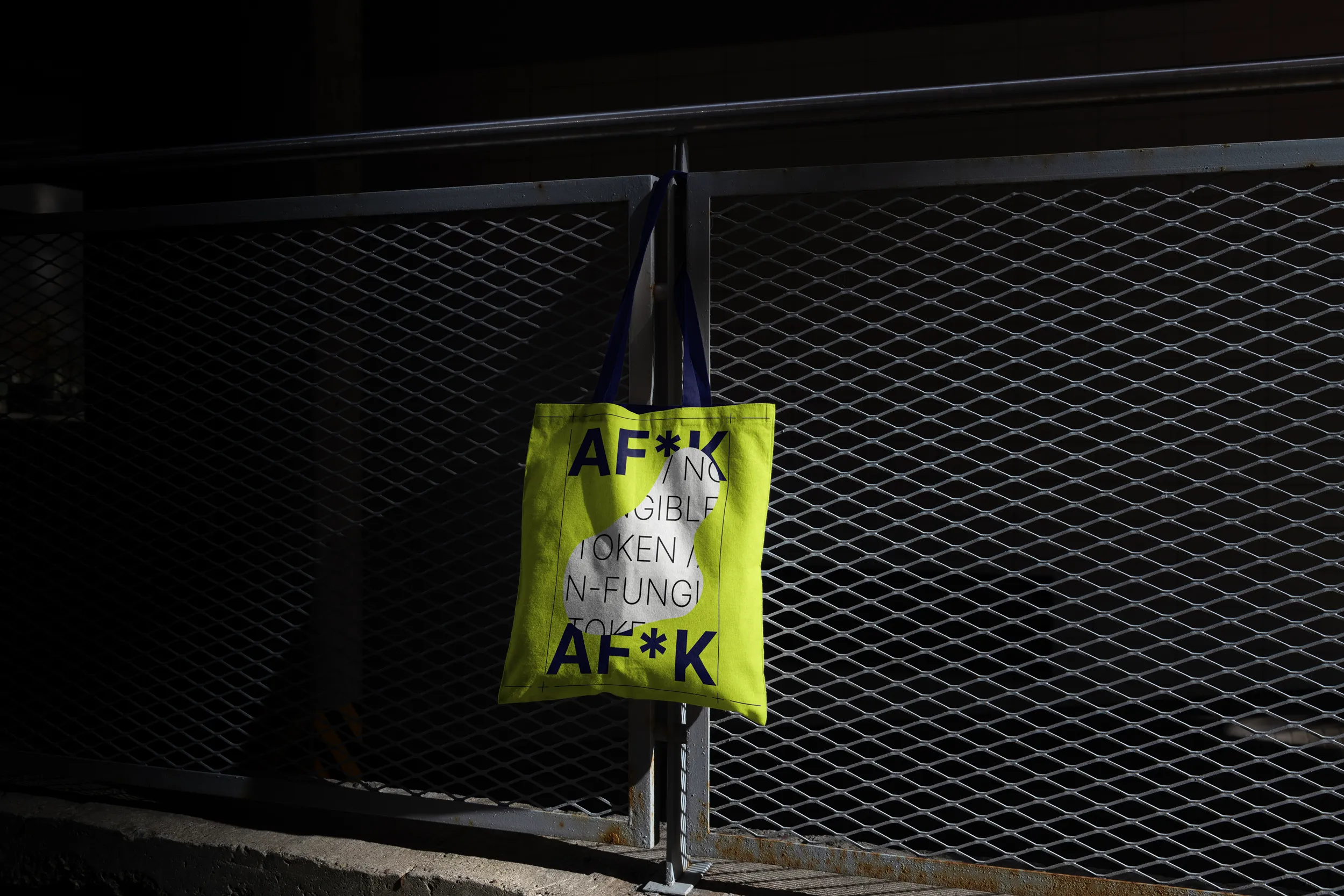 A AF*K branded tote bag hanging on a fence